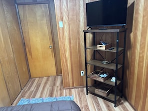 A room with a wooden door, a television on a metal stand, and a wooden floor. - Cozy, Affordable Retreat Near Anchorage Airport (Anchorage)