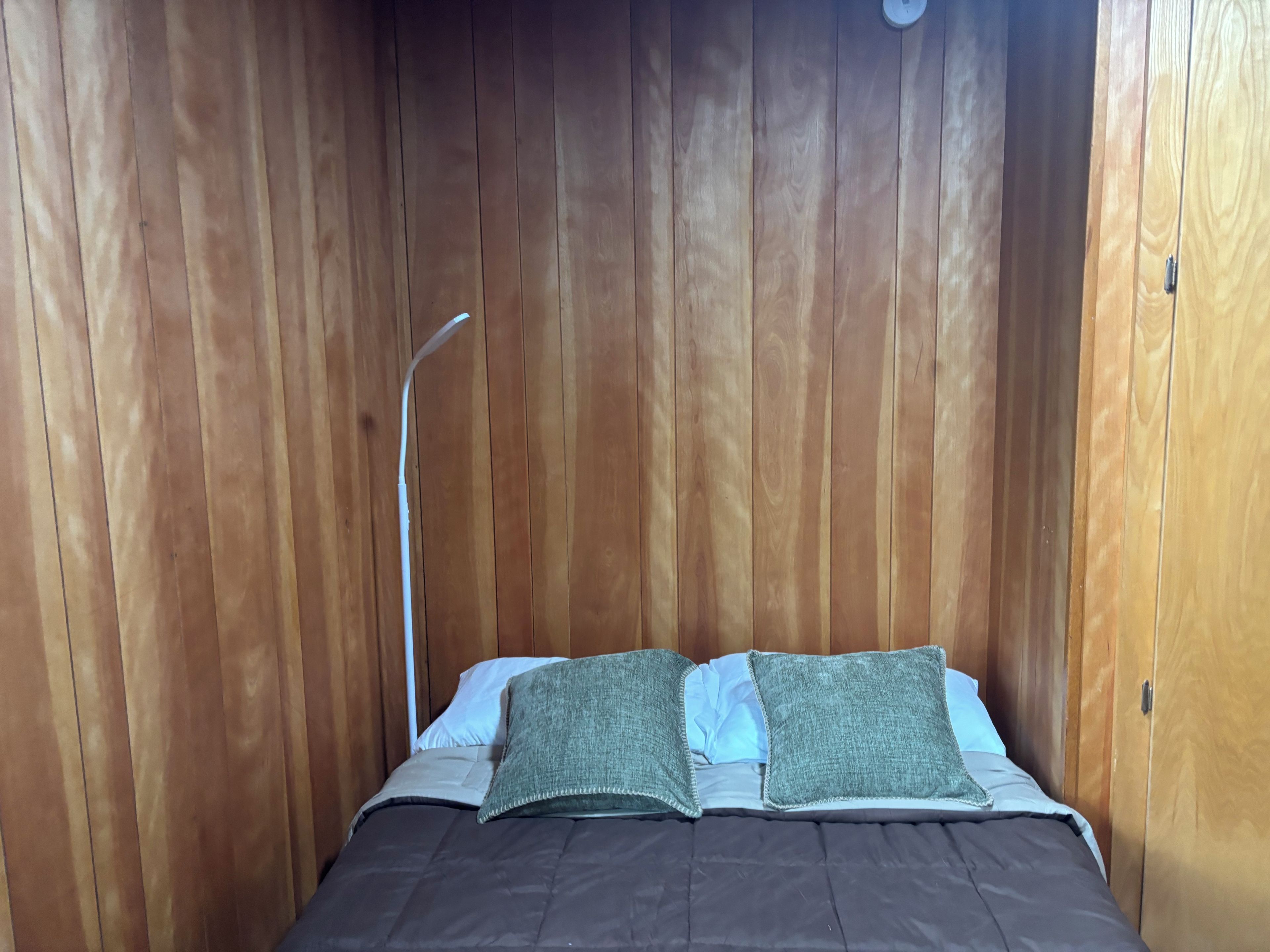 A wooden-paneled room with a bed, pillows, and a bedside lamp.