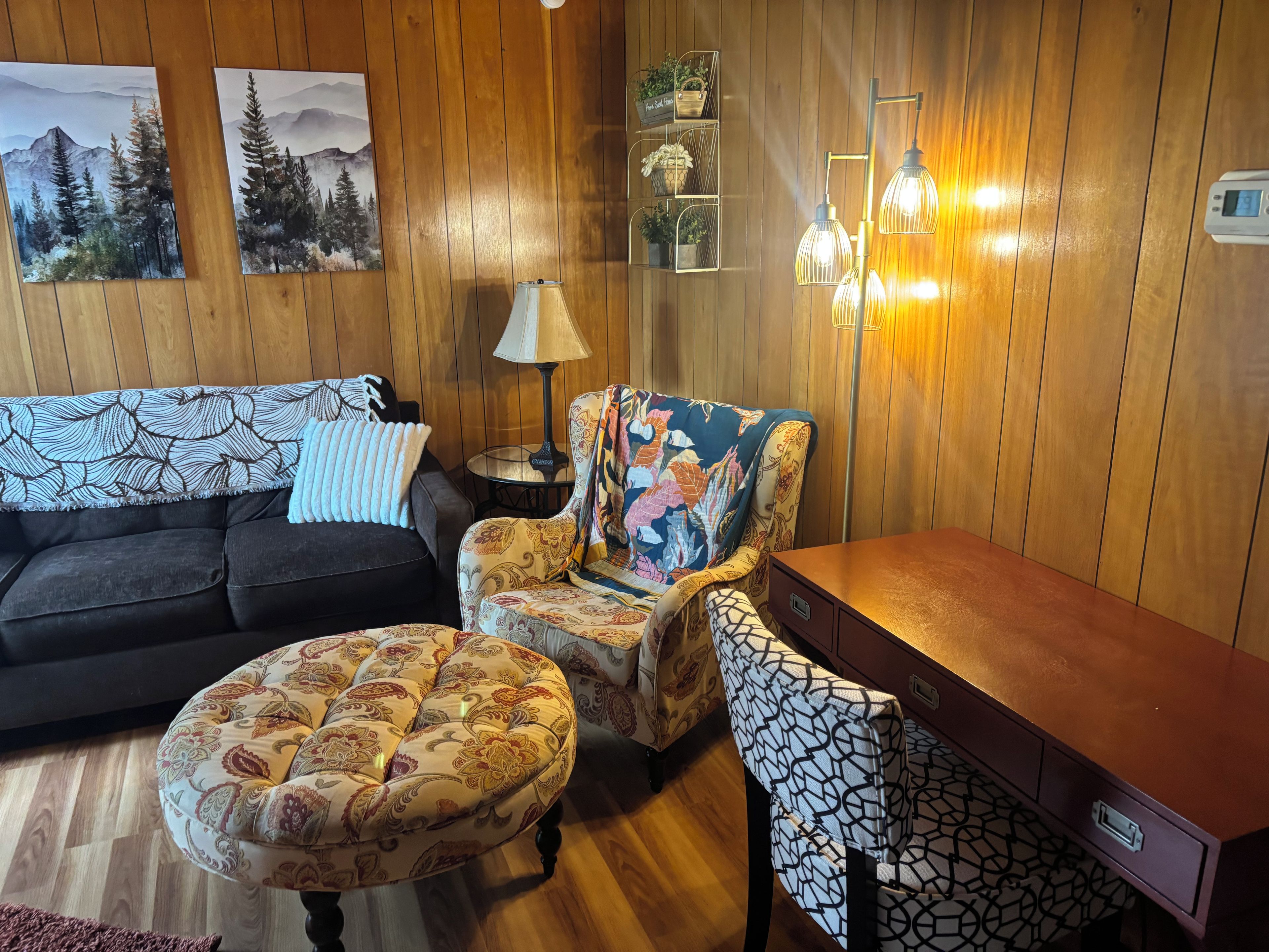 A cozy living room with a sofa, armchair, ottoman, and a wooden side table.