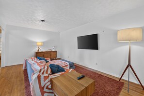 A modern bedroom with a bed, a bedside table, a lamp, a TV, and a floor lamp. - Sunshine City House (St. Petersburg)