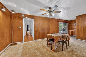 A room with a dining table, chairs, a ceiling fan, and a large window. - Sunshine City House (St. Petersburg)