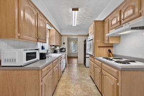 A kitchen with wooden cabinets, a microwave, stove, and a sink. - Sunshine City House (St. Petersburg)