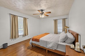 A bedroom with a bed, curtains, a ceiling fan, a bedside table with candles, and a window with blinds. - Sunshine City House (St. Petersburg)
