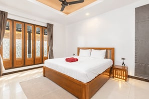 Ein Schlafzimmer mit einem hölzernen Bett, einem Deckenventilator, einem Nachttisch und einem großen Fenster mit Vorhängen.
