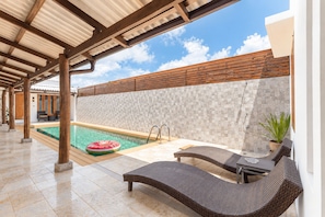 Un espace extérieur abrité comprenant une piscine, des chaises longues et une clôture en bois.