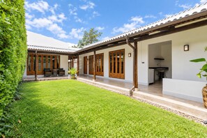 Ein Wohnhaus mit überdachter Terrasse, Rasenfläche und Küchenbereich.