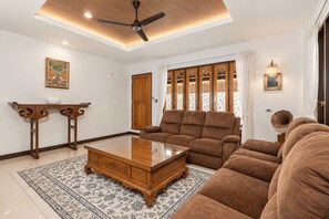 Ein Wohnzimmer mit Deckenventilator, einer Couch, einem Couchtisch, einem Schrank und einem gemusterten Teppich.