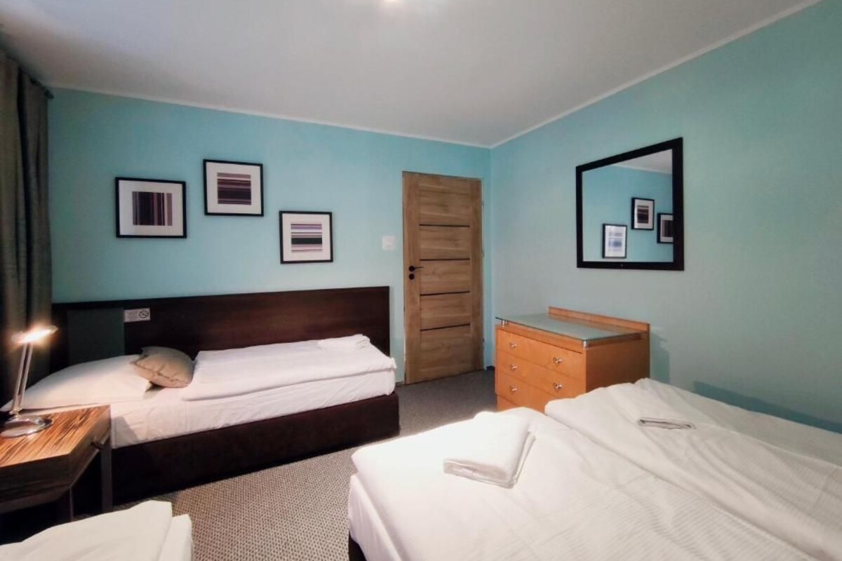 A hotel room with two beds, a wooden wardrobe, a dresser, and a mirror on the wall.