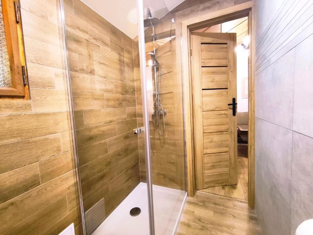 Une salle de bain avec des murs en bois, une douche en verre et une porte visible donnant sur une autre pièce.