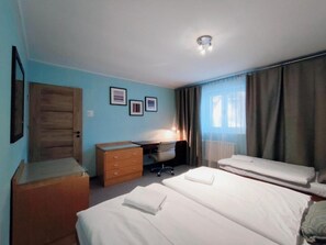 A hotel room with a bed, a desk, a chair, a dresser, and a door.