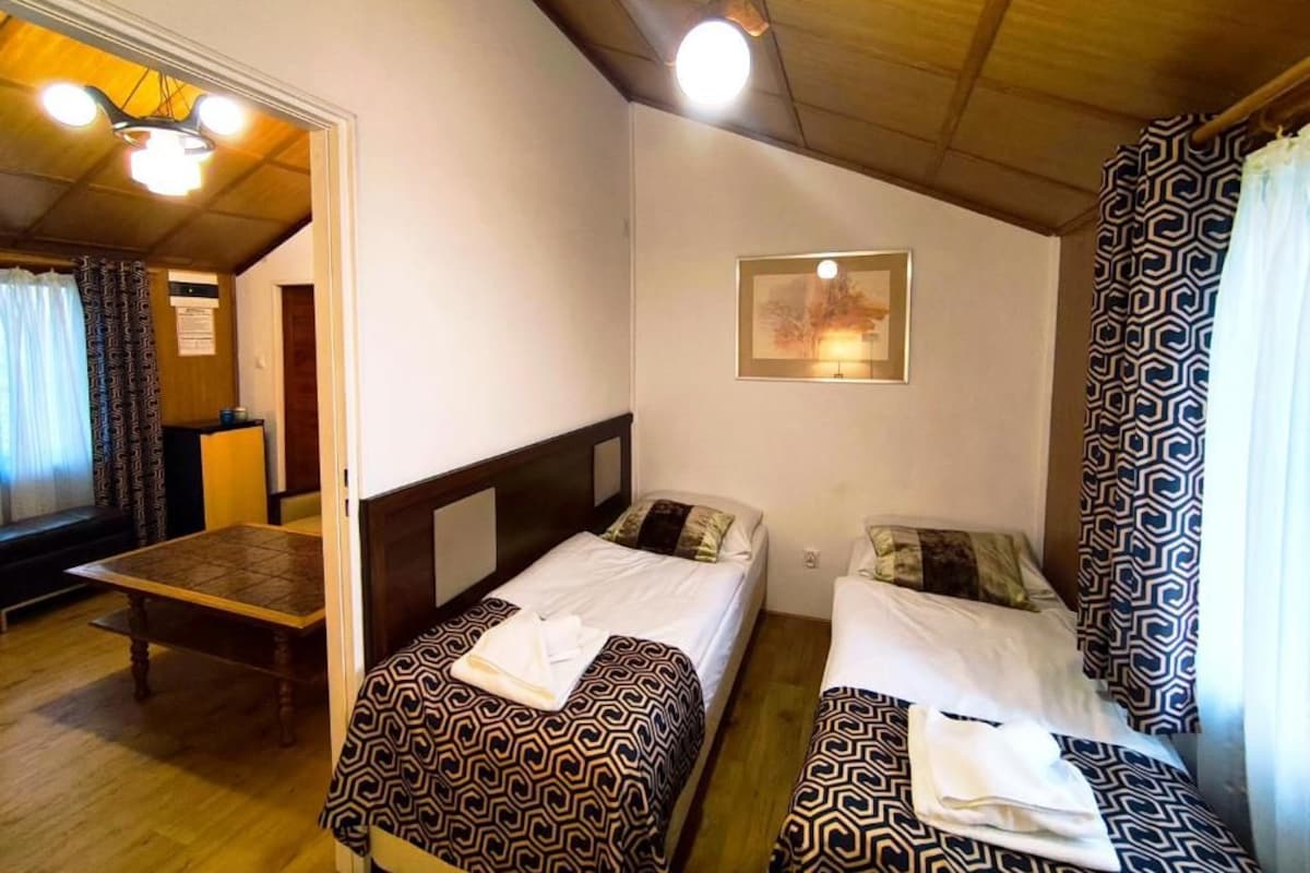 A room with two beds, a wooden table, and a ceiling light fixture.