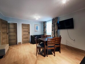 A dining area with a table and chairs, a sofa, a TV mounted on the wall, and a door.