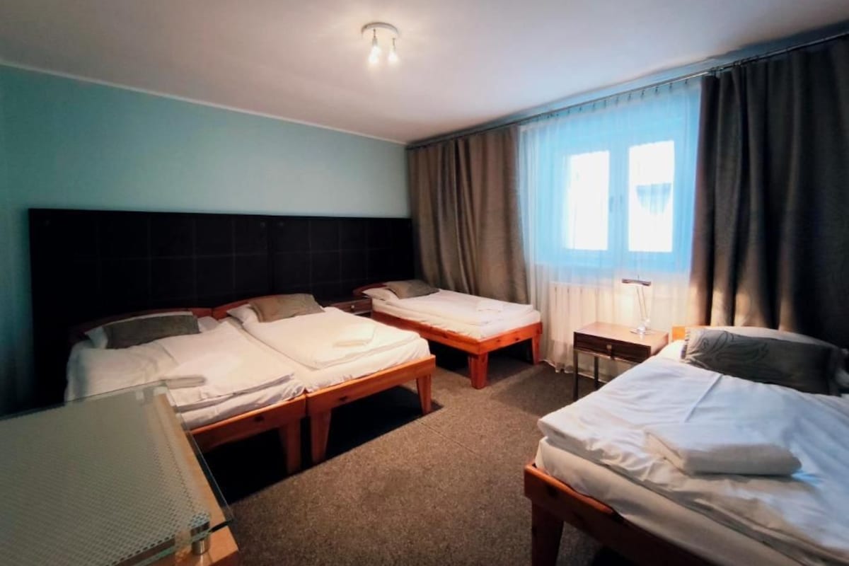 A hotel room with two single beds, a small table, a chair, and a window with curtains.