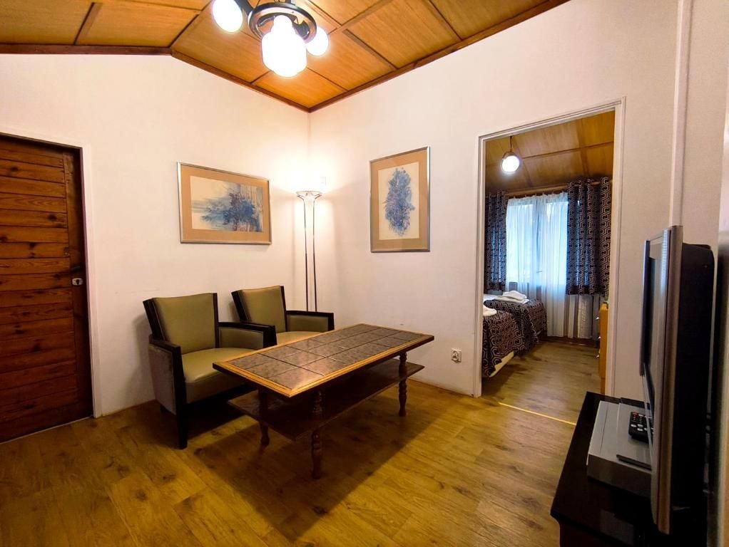 A room with a wooden floor, a sofa, a table, a lamp, and a television.
