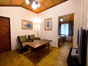 Una habitación con suelo de madera, un sofá, una mesa, una lámpara y un televisor.