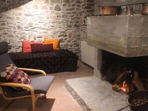 A stone-walled room with a fireplace, a bed with patterned bedding, and a chair with a colorful cushion. - Casa al Portico by Interhome (Novaggio)