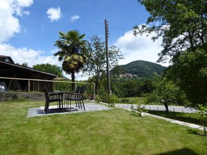 A grassy outdoor area with a table and chairs, a palm tree, and a mountain in the background. - Casa al Portico by Interhome (Novaggio)