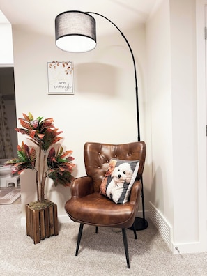 A brown leather chair with a dog-themed pillow, a tall floor lamp, a framed inspirational quote, and a potted plant with red and green leaves. - Private Suite Near Calgary Airport (Calgary)