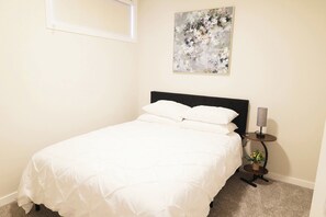 A neatly made bed in a room with a single bedside table, a lamp, and a painting on the wall. - Private Suite Near Calgary Airport (Calgary)