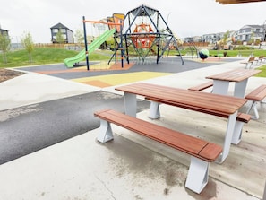A playground with a slide, swings, and a climbing structure. There are picnic tables and benches in the foreground. - Private Suite Near Calgary Airport (Calgary)