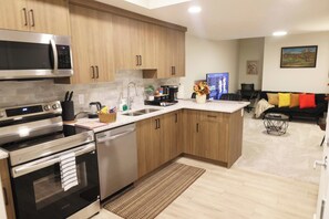 A modern kitchen with stainless steel appliances, wooden cabinets, and a central island with a sink. - Private Suite Near Calgary Airport (Calgary)