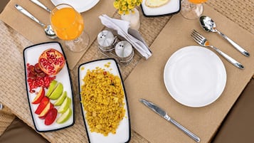 Un desayuno con un plato de fruta, un tazón de arroz amarillo, un vaso de jugo de naranja y una taza de café.