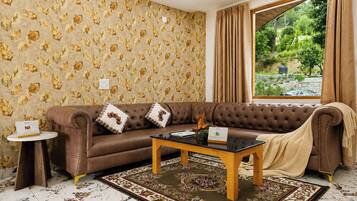 A room with a brown leather sofa, a glass coffee table, a patterned rug, and a window with curtains.
