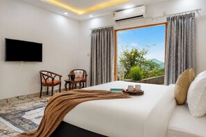 A hotel room with a bed, a flat-screen TV, two chairs, a window with curtains, and an air conditioning unit. - ELIVAAS Signature SECRET ESCAPE SWARAN (Solan)