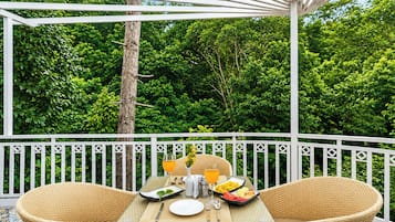 Un área de comedor al aire libre con muebles de mimbre, una mesa lista para dos personas y vistas a follaje exuberante.