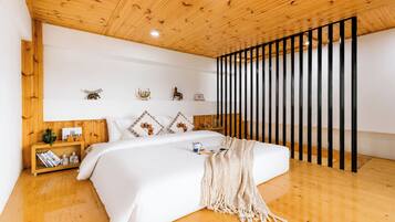 Une chambre avec un plafond en bois, un lit recouvert de linge de lit blanc, une table de chevet avec des livres et une plante, et une étagère murale ornée d’objets décoratifs.
