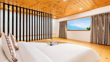A bedroom with a large bed, wooden ceiling, black railing, and a window with a mountain view.