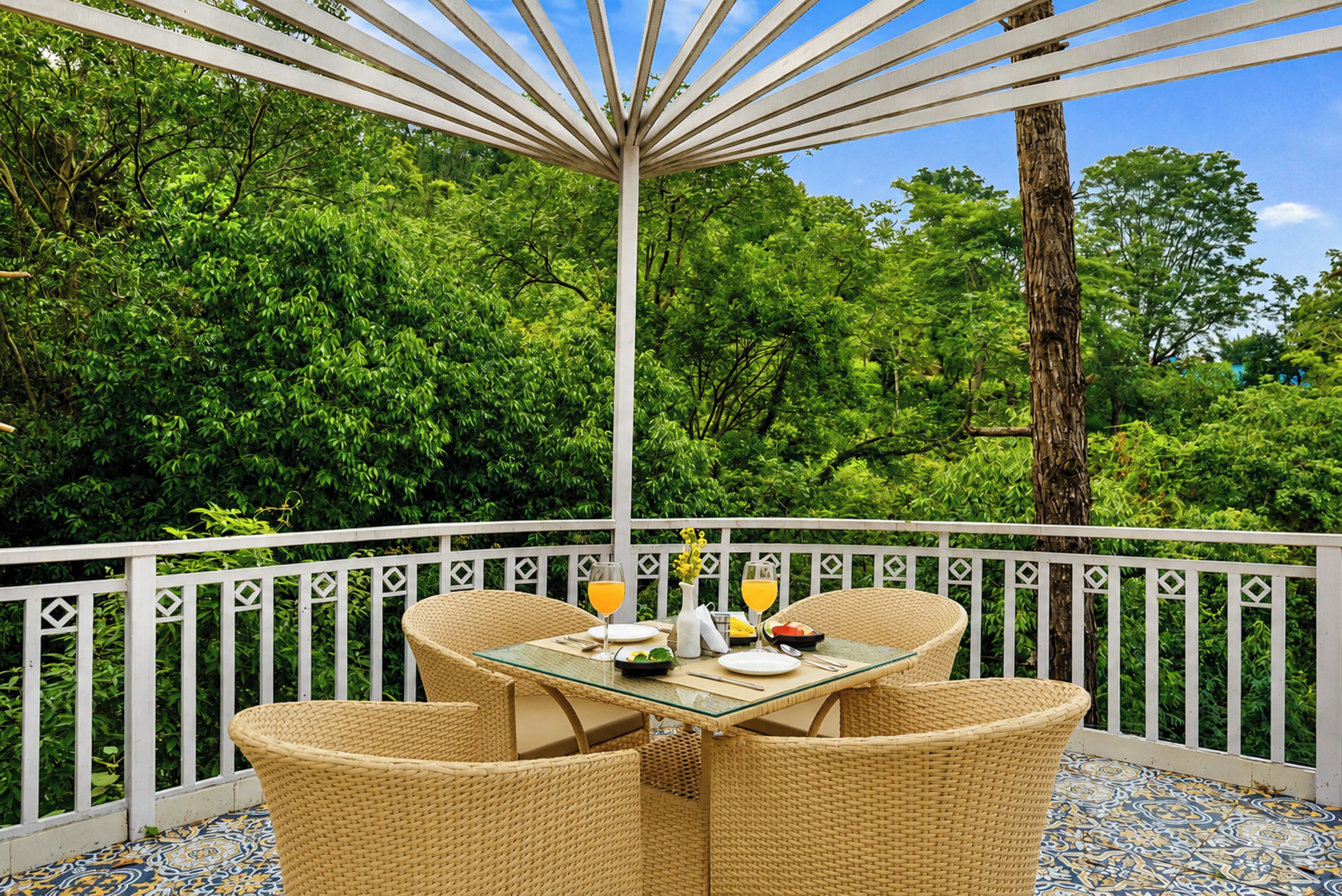 A covered outdoor dining area with wicker furniture and a table set for two, overlooking a lush green landscape.