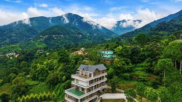 A multi-story building with a green roof, surrounded by lush greenery and mountains in the background.