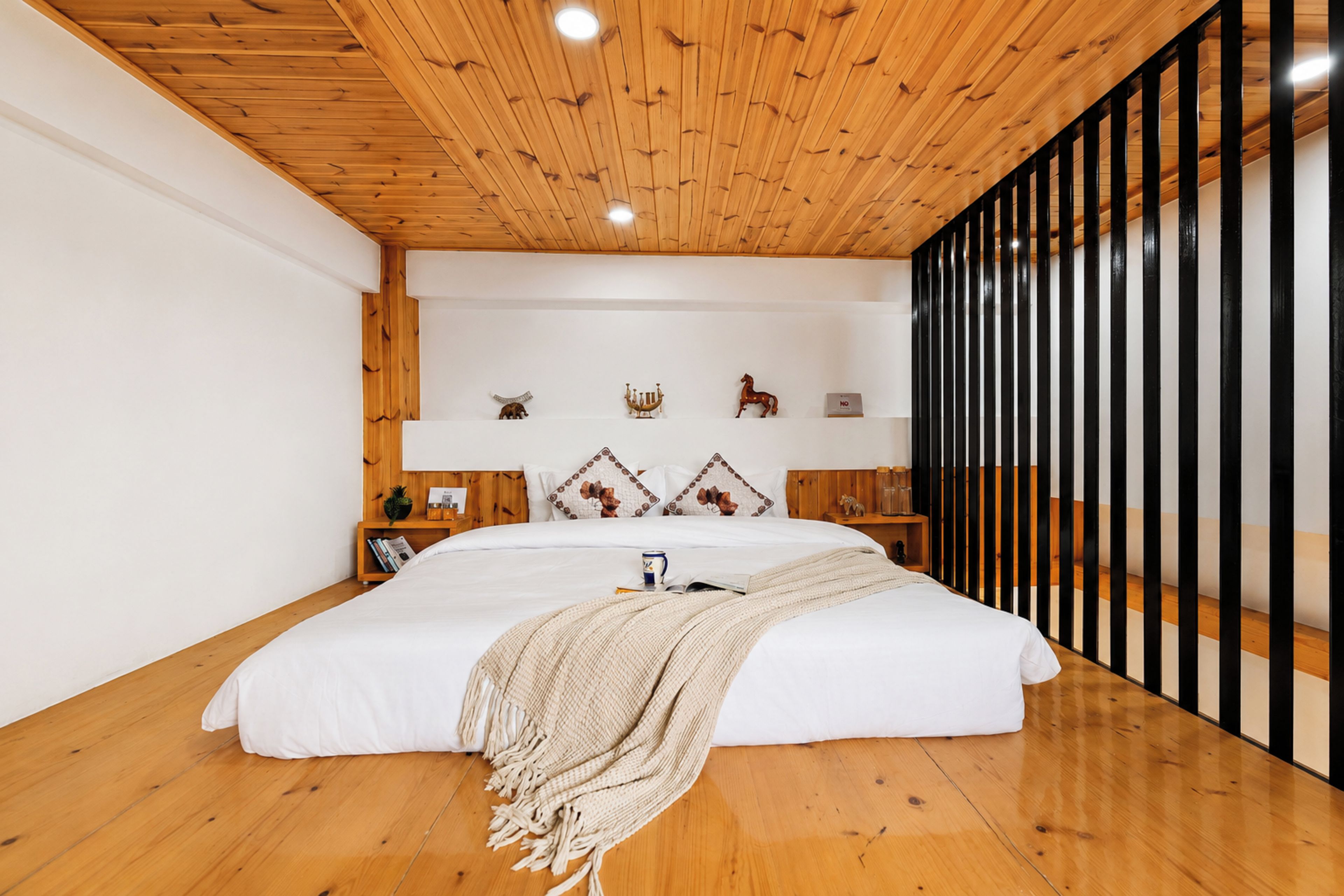 Ein Schlafzimmer mit einem großen Bett, Holzbalkendecke, weißen Wänden und einer schwarzen Trennwand.