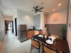 A modern kitchen with a refrigerator, stove, and sink. There is a dining area with a table set for two and a ceiling fan. - Neu suite Family Room By Rasbo Galaxy (Kuala Lumpur)