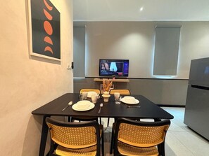 Ein Essbereich mit Tisch für vier Personen, einem Fernseher an der Wand und einer Küche im Hintergrund.