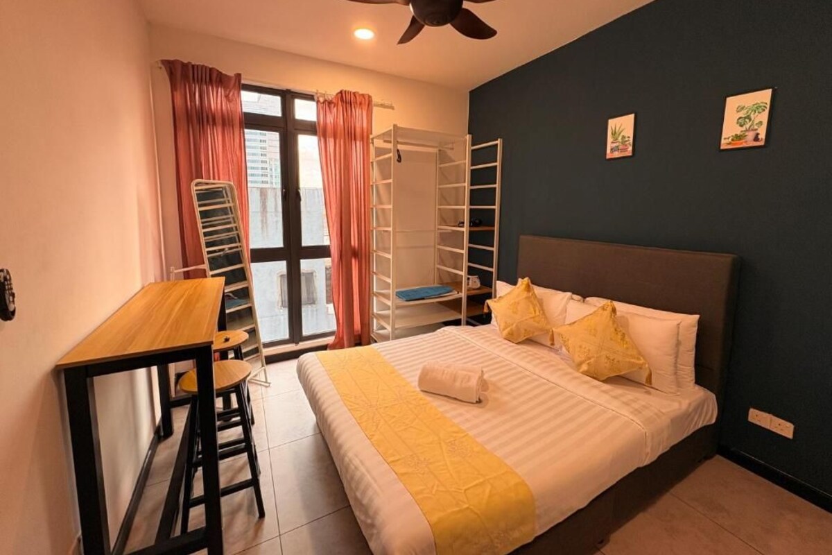 Ein Schlafzimmer mit einem Bett, einem Schreibtisch, einem Stuhl, einem Deckenventilator und einem Fenster mit Vorhängen.