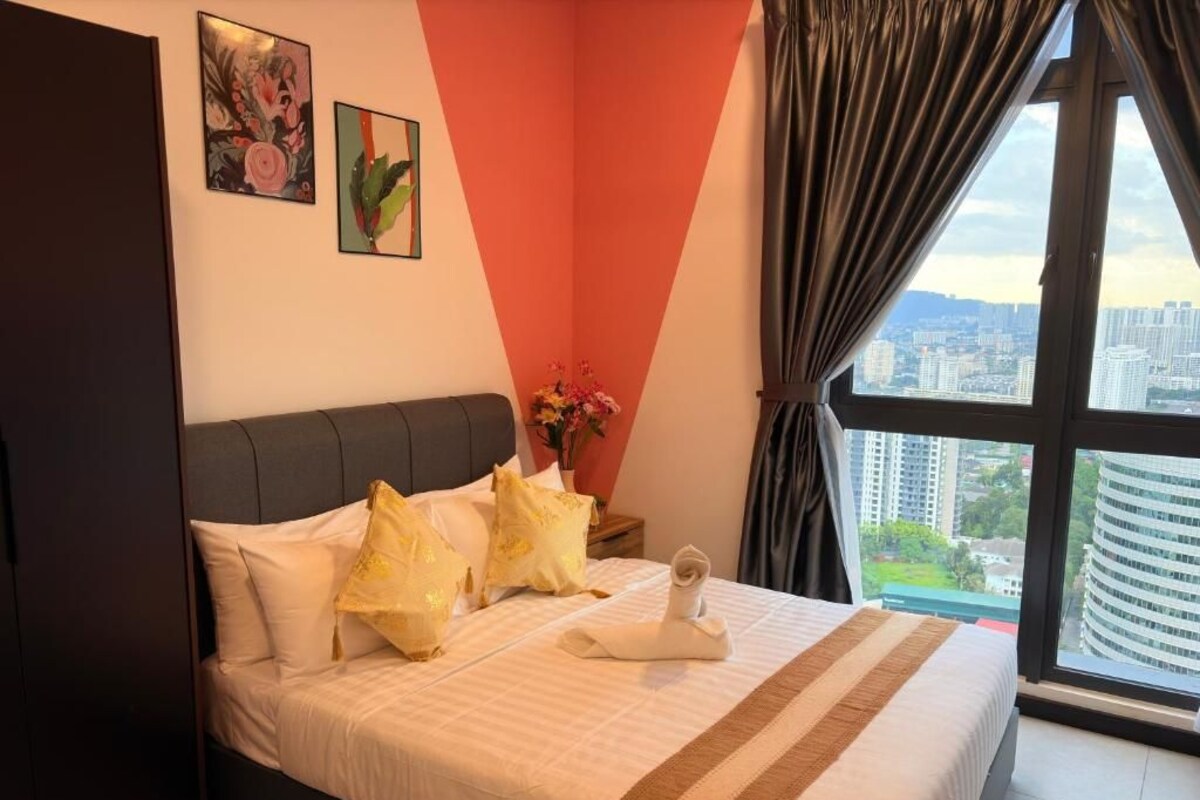Ein Hotelzimmer mit Bett, Nachttisch, Blumen in einer Vase und Blick auf die Stadt durch das Fenster.
