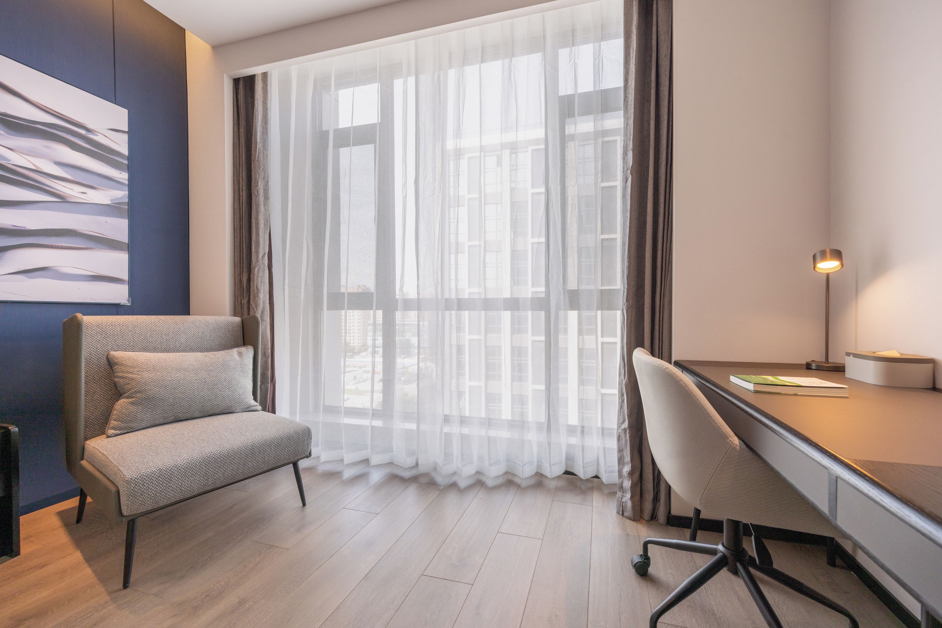 A modern room with a desk, chair, and a large window with sheer curtains.