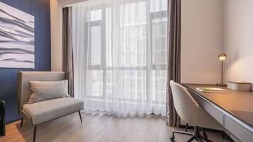 A modern room with a desk, chair, and a large window with sheer curtains.