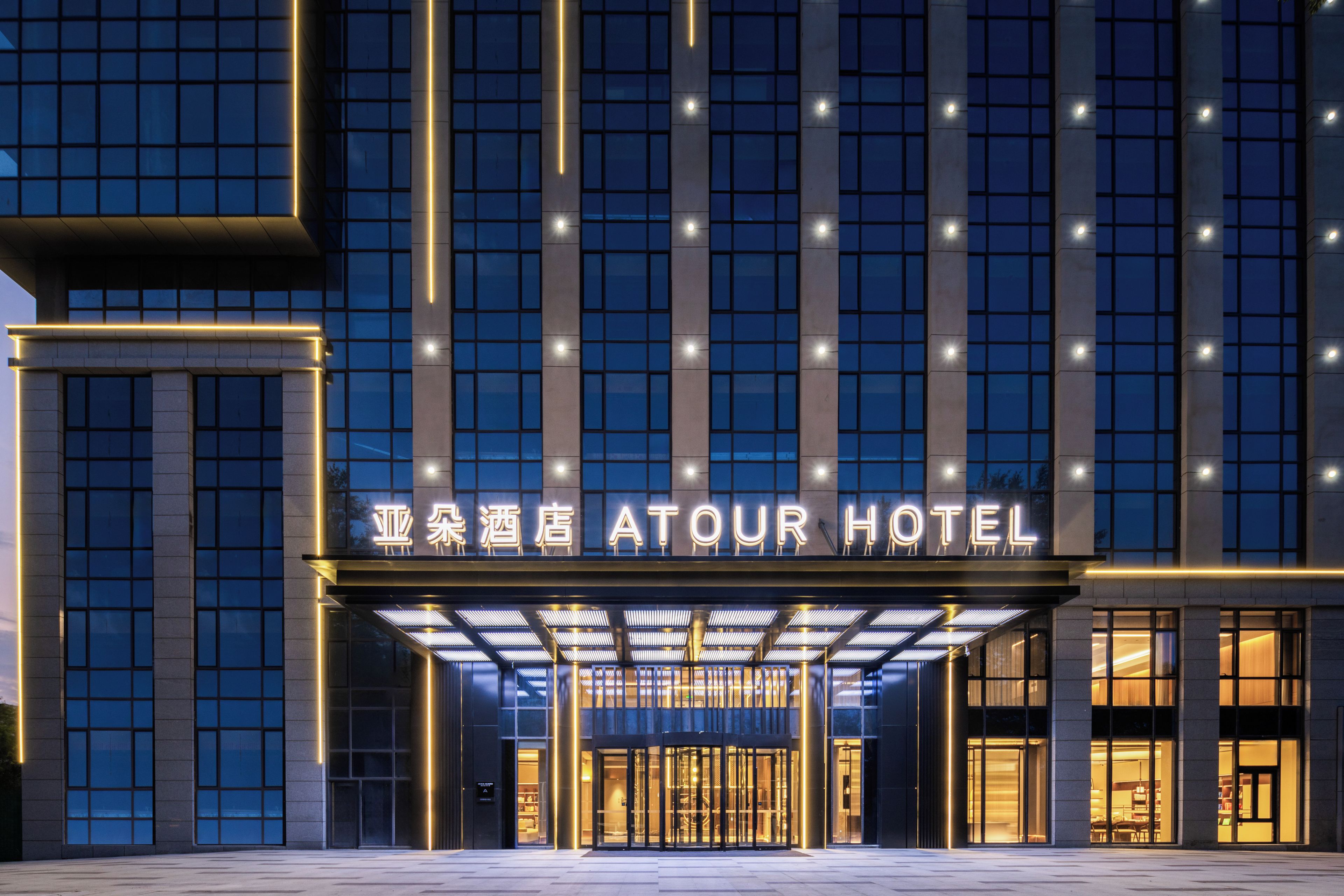 Fachada moderna de un hotel con señalización iluminada y un área de acceso cubierta.