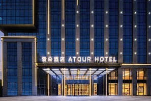 Een hotelentree met een moderne gevel, verlichte borden en een overdekt gedeelte.