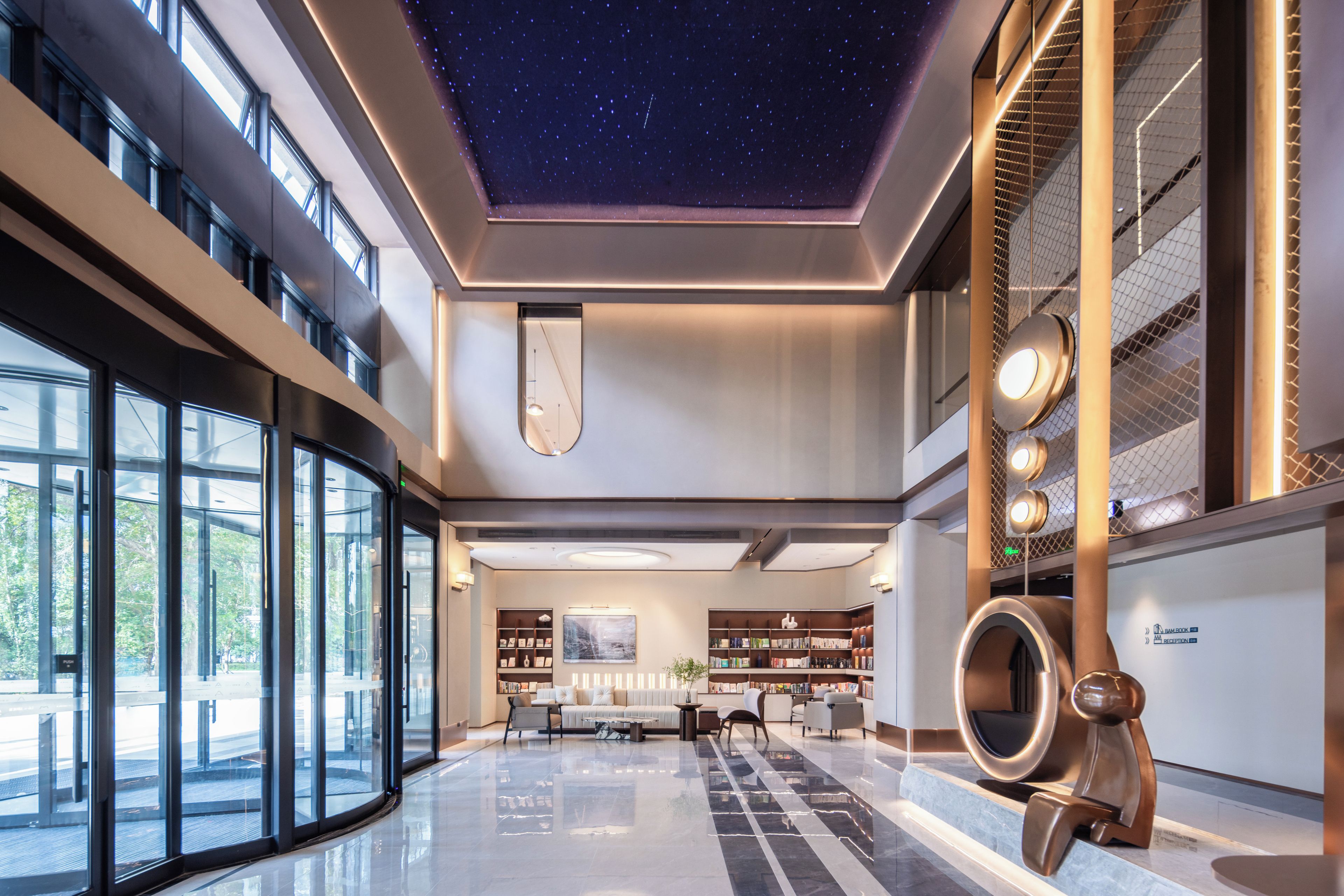 A spacious lobby with a starry ceiling, a reception desk, and a seating area with bookshelves.