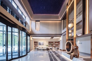 Un vestíbul espaiós amb un sostre estrellat, una taula de recepció i una zona de seients amb prestatgeries.