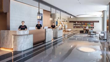 A hotel reception area with marble counters, a seating area with a sofa and chairs, and a bookshelf with various items.