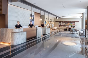 Een hotel receptie met marmeren balies, een zithoek met een bank en stoelen, en een boekenplank met diverse spullen.