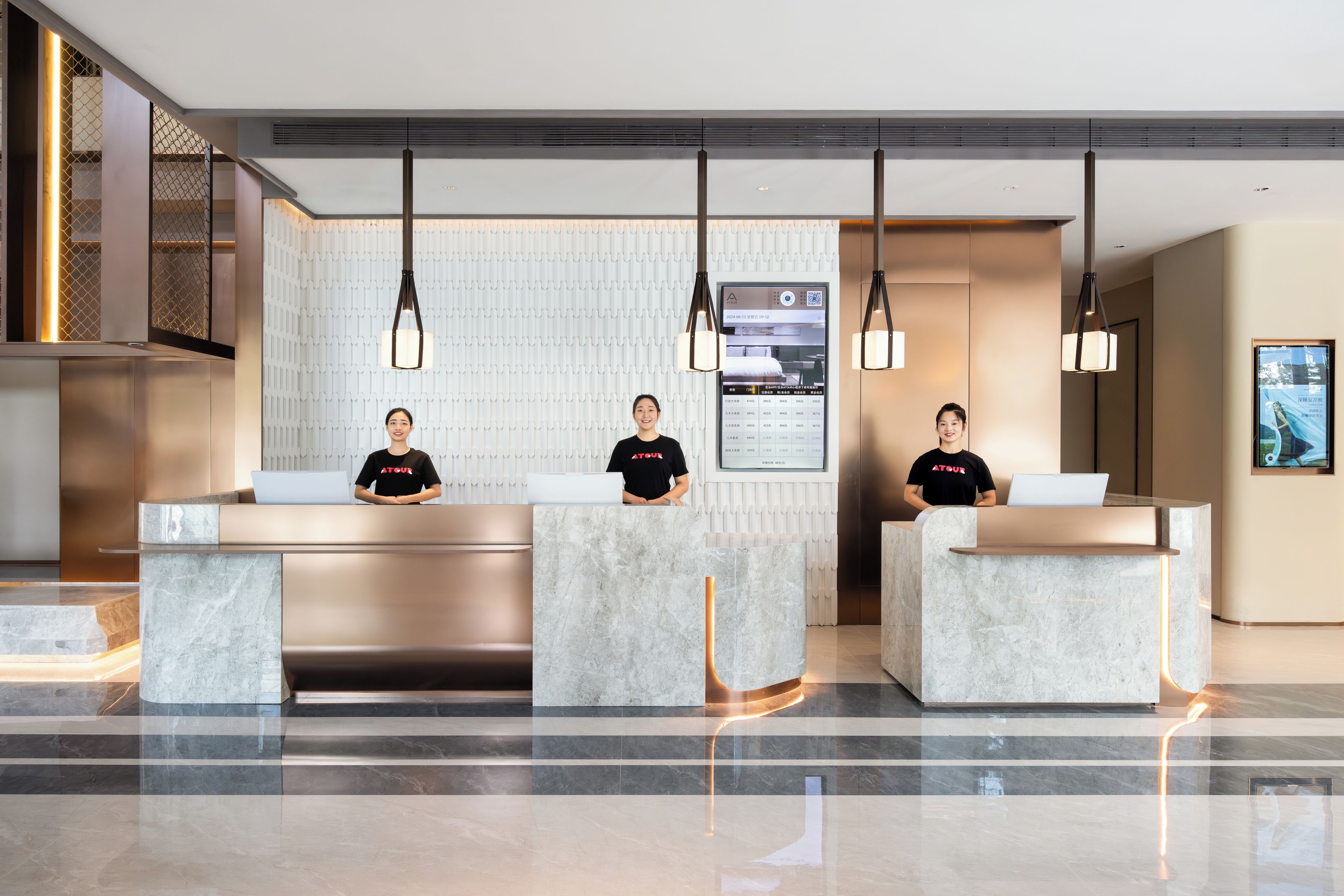 A hotel reception area with three receptionists, marble reception desks, and modern pendant lighting.