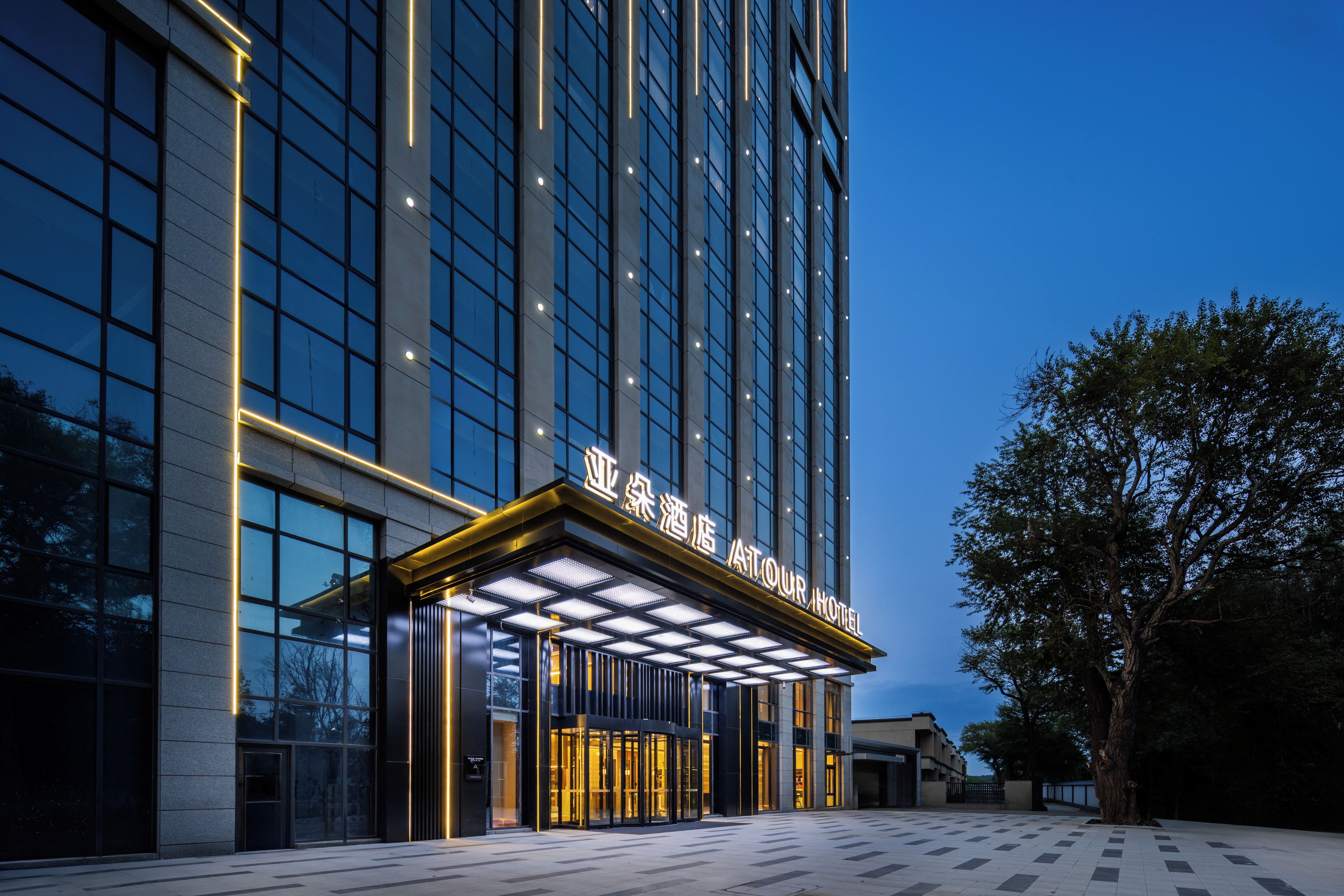 Ein moderner Hotel Eingang mit Glasfassade und beleuchteter Beschilderung.
