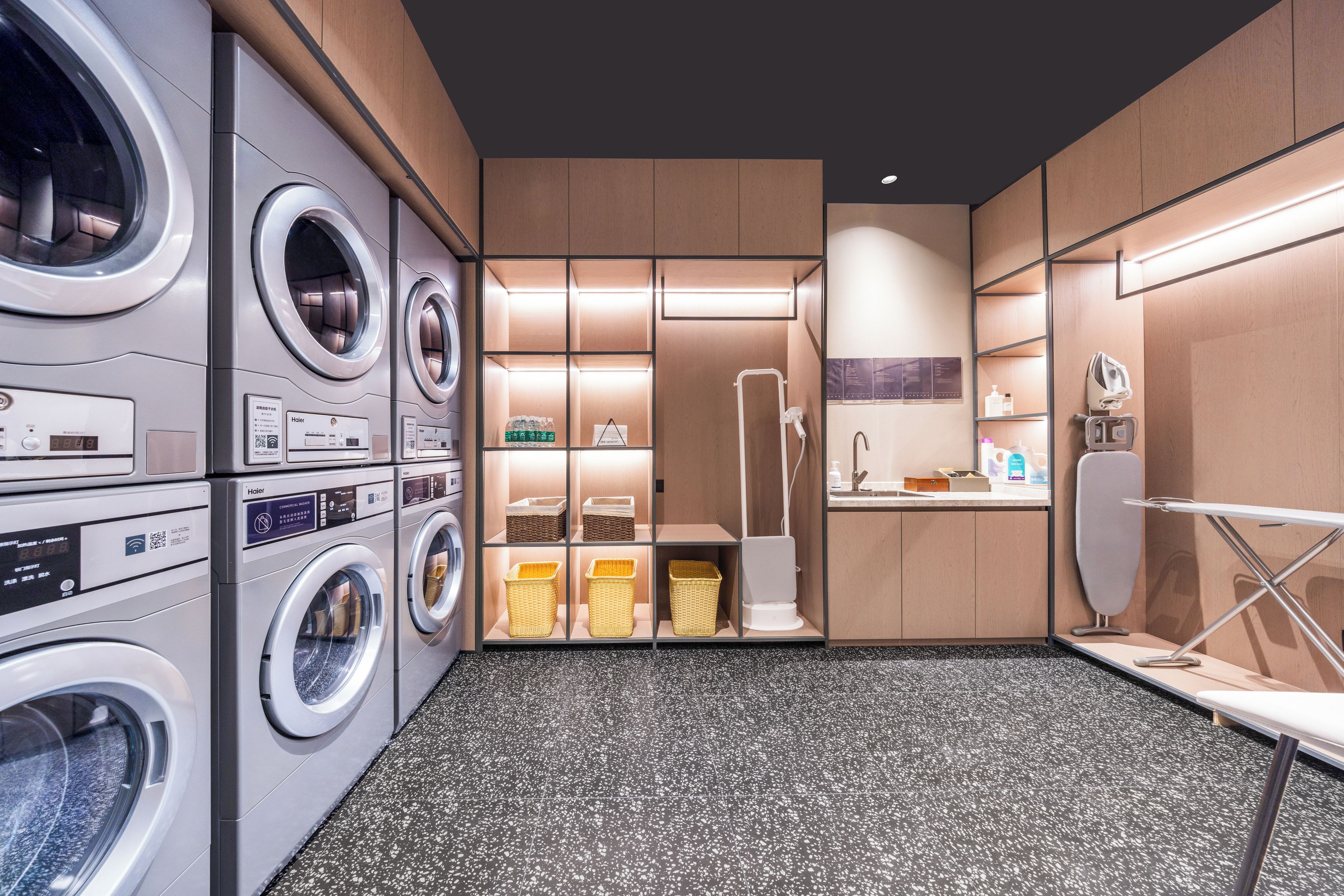 Un cuarto de lavandería con varias lavadoras comerciales Haier, un tendedero y un espacio pequeño con lavamanos.