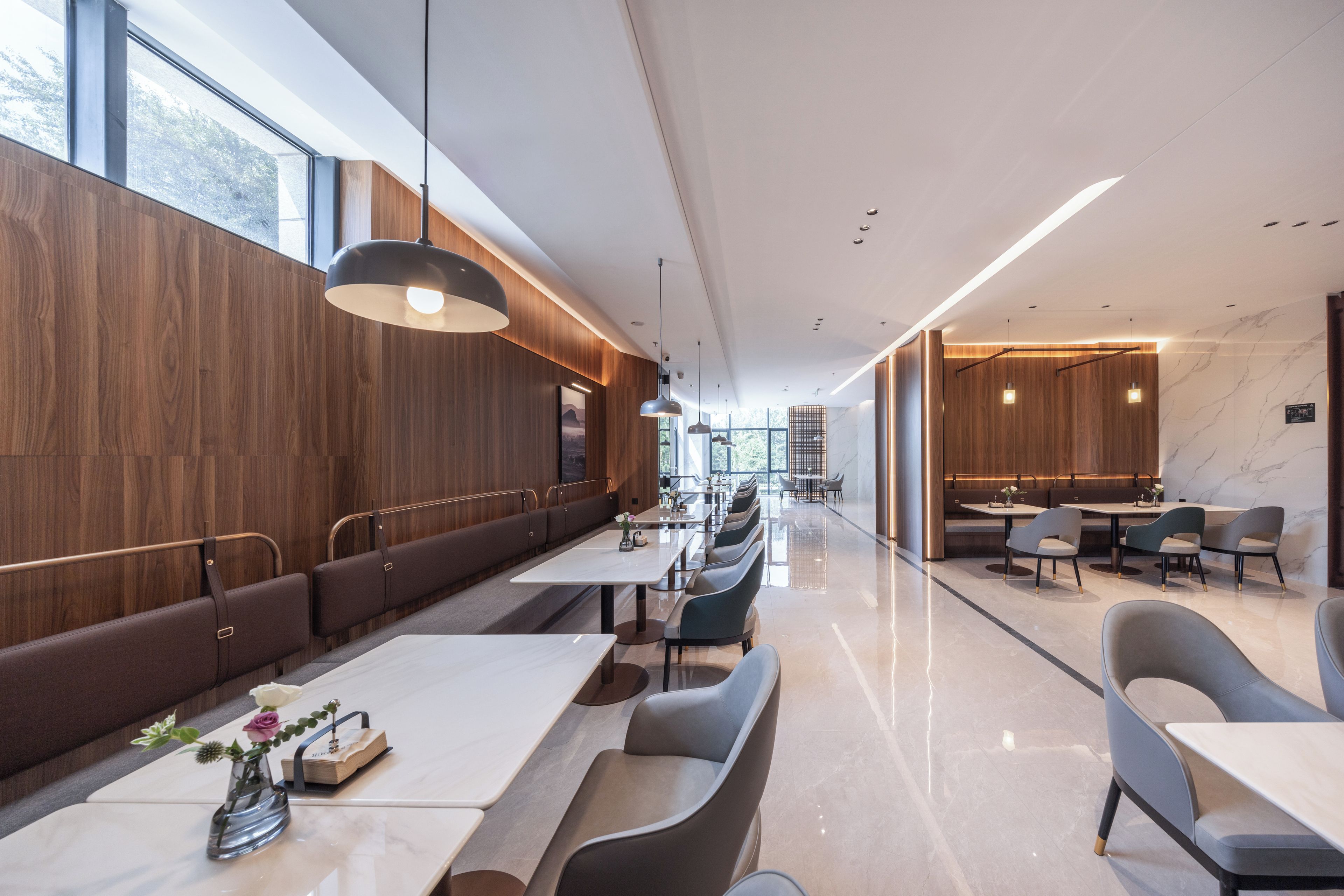A modern restaurant with long communal tables and booths, wooden paneling, and a marble floor.